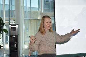 Bilde av Lisa Blom. Som sansylighvis snakker foran publikum og har på seg genser i lyse brun farge.